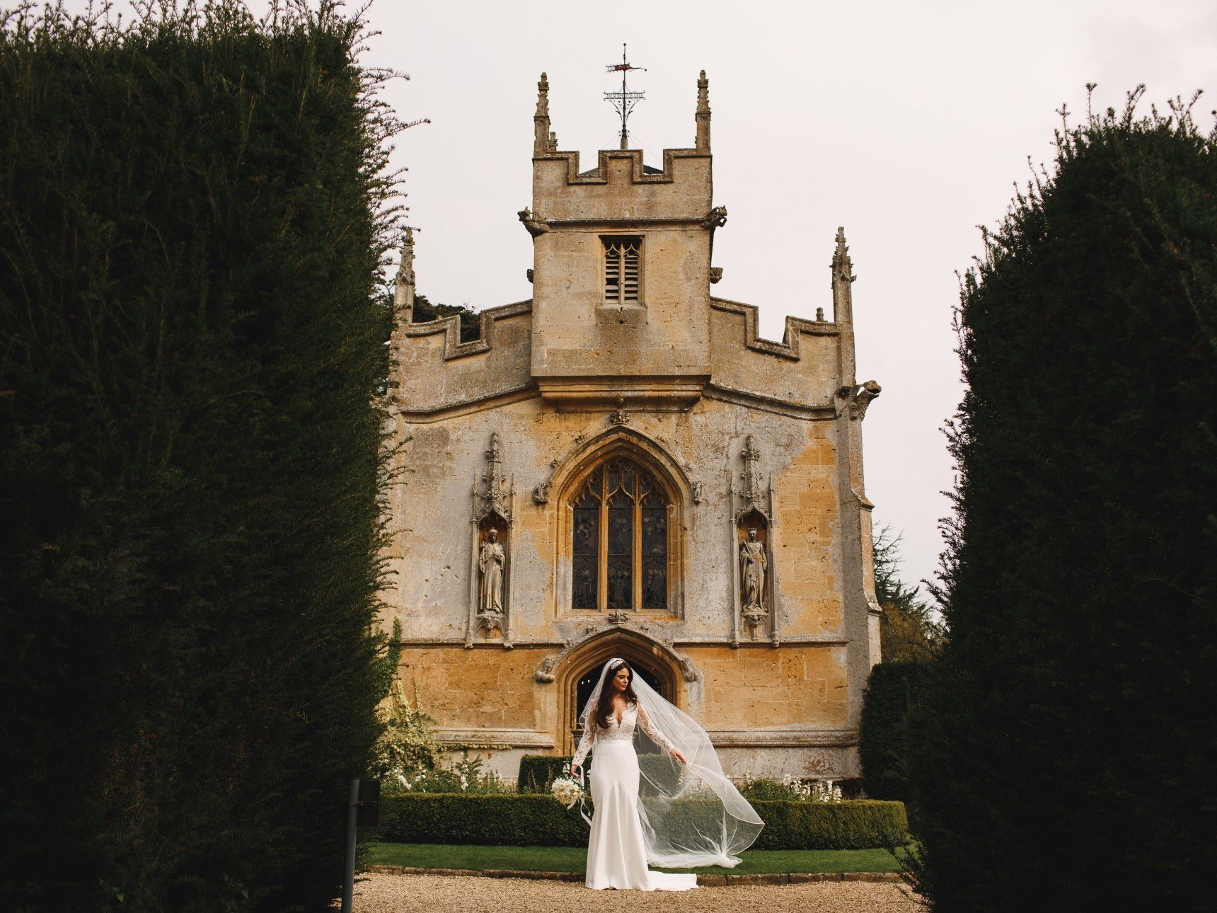 Bride poses outside church viewed between hedges